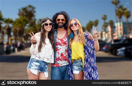 summer holidays, youth culture, gesture and people concept - smiling young hippie friends in sunglasses showing peace hand sign over venice beach in los angeles background. hippie friends showing peace at venice beach in la