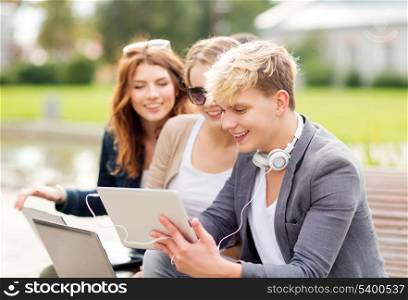 summer, internet, education, campus and teenage concept - group of students or teenagers with laptop and tablet computers hanging out
