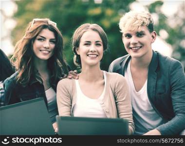 summer, internet, education, campus and teenage concept - group of students or teenagers with laptop computers hanging out