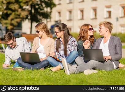 summer, internet, education, technlogy and campus concept - group of students or teenagers with laptop, notebooks, files and folders
