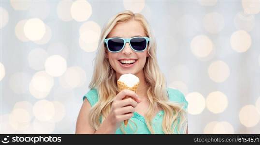 summer, junk food and people concept - young woman or teenage girl in sunglasses eating ice cream over holidays lights background