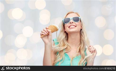 summer, junk food and people concept - young woman or teenage girl in sunglasses eating ice cream over holidays lights background