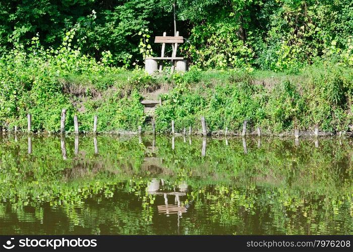 Summer lake with trees reflection on water surface and bench on shore.