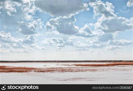Summer landscape - lake among the reeds in the pit of quartz sand with a remote horizon and beautiful cloudy sky.. Lake Among Quartz Sand Under Beautiful Cloudy Sky