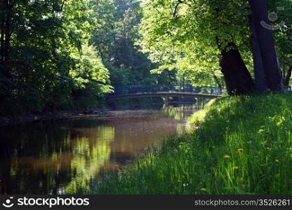 Summer landscape - small silent river, bridge, rays of sunlight and many-many green