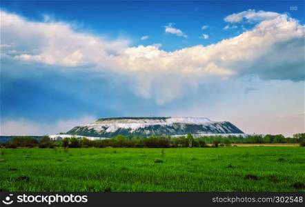 Summer landscape with green field and beautiful cumulus clouds over the white gypsum mountain. Russia, Moscow region, Voskresensky district.. Field Landscape With Cumulus Clouds Over The White Mountain