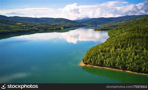 Summer landscape with lake and mountain woodland. Reflection of sky, clouds, forest and mountains in water. Aerial view of Reservoir/lake Starina, Poloniny national park, Slovakia.