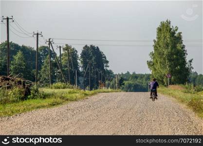 Summer landscape with road, trees and blue sky. Man ride to the moped on countryside road. Rural road, cornfield, wood and cloudy blue sky. Classic rural landscape in Latvia.