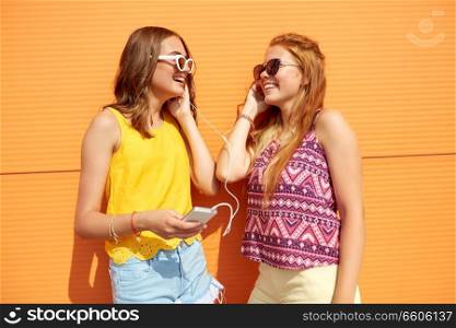 summer, leisure and technology concept - smiling teenage girls in sunglasses and earphones listening to music from smartphone outdoors. teenage girls listening to music from smartphone