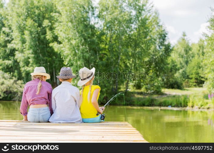 Summer leisure. Rear view of three children sitting at bank and fishing