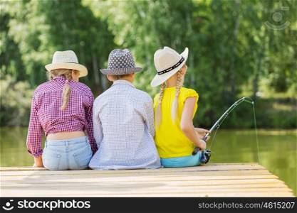 Summer leisure. Rear view of three children sitting at bank and fishing