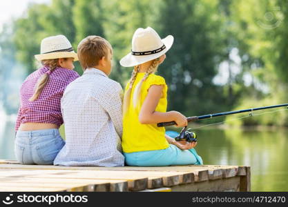 Summer leisure. Rear view of three children sitting at bank and fishing