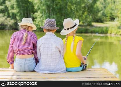 Summer leisure. Rear view of three children sitting at bank and fishing