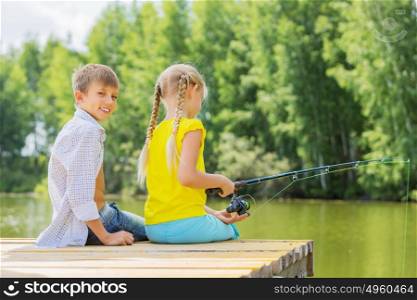 Summer leisure. Rear view of two children sitting at bank and fishing