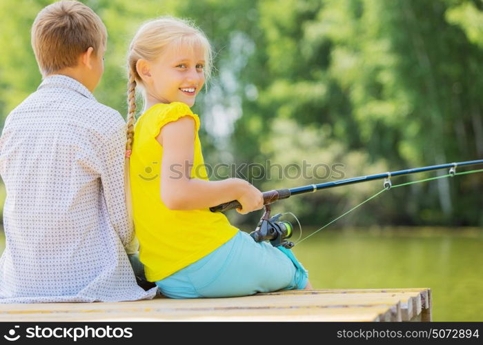 Summer leisure. Rear view of two children sitting at bank and fishing