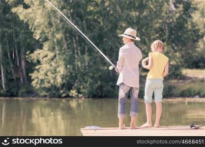 Summer leisure. Rear view of two children standing at bank and fishing