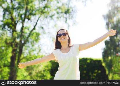 summer, leisure, vacation and people concept - smiling young woman wearing sunglasses standing in park