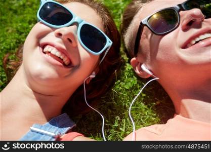 summer, love and people concept - close up of happy teenage couple in sunglasses lying on grass with earphones and listening to music