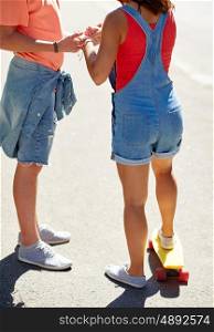 summer, love, extreme sport and people concept - close up of teenage couple riding short modern cruiser skateboard on city street
