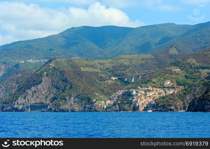 Summer Manarola view from excursion ship. One of five famous villages of Cinque Terre National Park in Liguria, Italy, suspended between Ligurian sea and land on sheer cliffs. People unrecognizable.