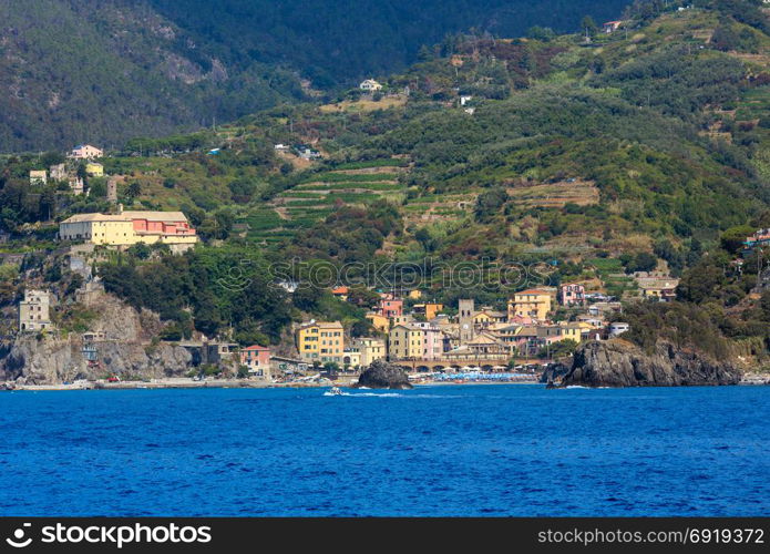 Summer Monterosso view from excursion ship. One of five famous villages of Cinque Terre National Park in Liguria, Italy, suspended between sea and land on sheer cliffs. People unrecognizable.