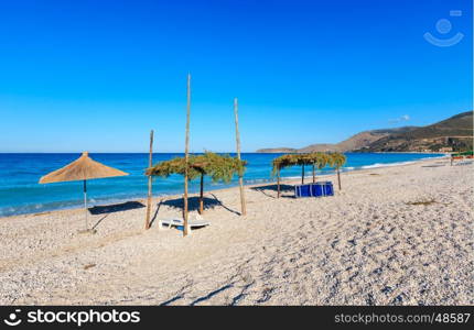 Summer morning pebbly beach with sunbeds and canopy (Borsh, Albania).