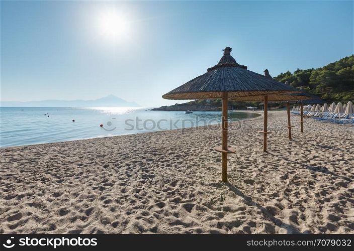 Summer morning Platanitsi beach with sunbeds and strawy sunshades (Chalkidiki, Greece).