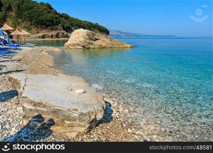 Summer morning Pulebardha beach with sunbeds, strawy sunshades and pebble (Saranda, Albania).
