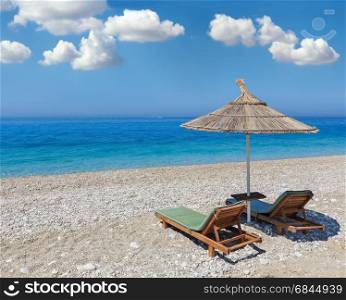 Summer morning sandy beach with sunbeds and strawy sunshade (Albania). Deep blue sky with some cumulus clouds.