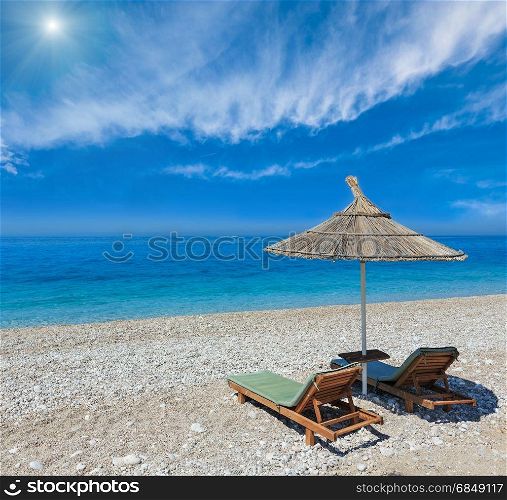 Summer morning sandy beach with sunbeds and strawy sunshade (Albania). Blue sky with some clouds and sunshine.