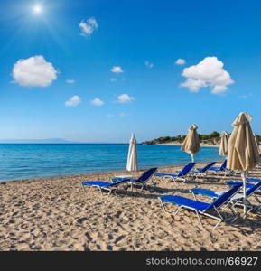 Summer morning sandy Platanitsi beach with sunbeds and sunshades (Halkidiki, Greece) and blue sunshiny sky above.
