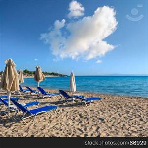 Summer morning sandy Platanitsi beach with sunbeds and sunshades (Halkidiki, Greece) and deep blue cloudy sky.
