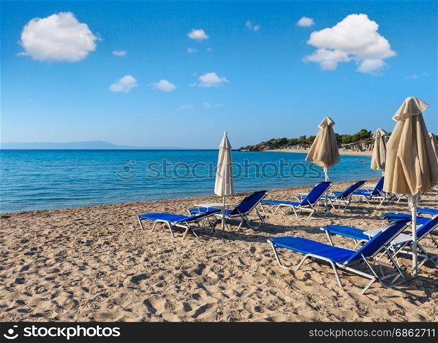Summer morning sandy Platanitsi beach with sunbeds and sunshades (Halkidiki, Greece) and blue sky above.