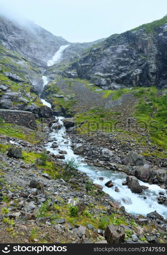 Summer mountain cloudy view with waterfall on slope (Norway).