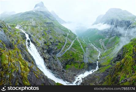 Summer mountain cloudy view with waterfall on slope (Norway).