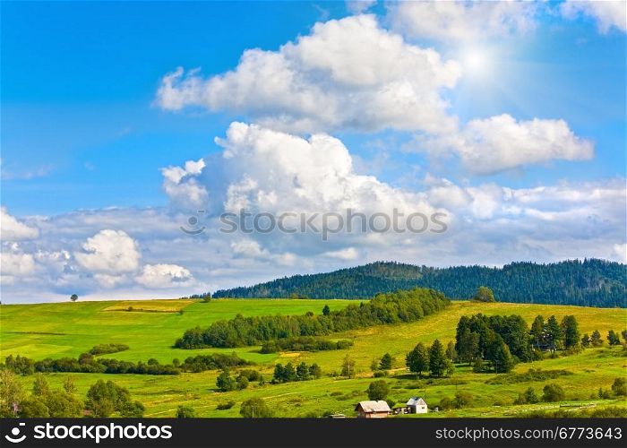 Summer mountain view with village outskirts and sunshine in blue sky