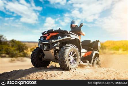 Summer offroad adventure on atv in sand quarry. Male rider in helmet on quad bike in sandpit
