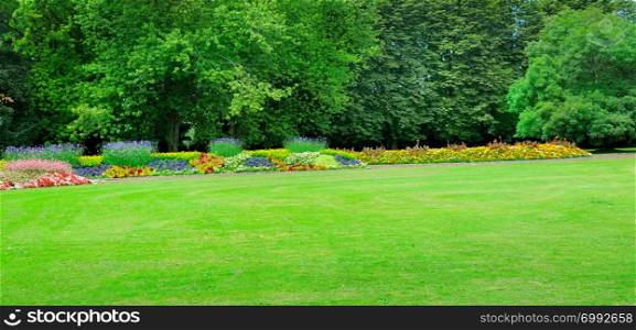 Summer park with beautiful flowerbeds and meadow. Wide photo.