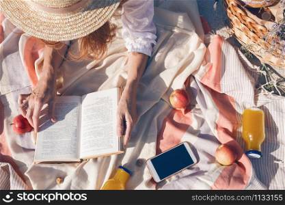 Summer - picnic by the sea. basket for a picnic with with buns, apples and juice. girl on a picnic lies and reads a book