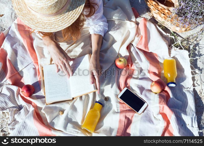 Summer - picnic by the sea. basket for a picnic with with buns, apples and juice. girl on a picnic lies and reads a book