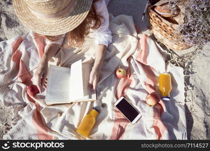 Summer - picnic by the sea. basket for a picnic with with buns, apples and juice. girl on a picnic lies and reads a book