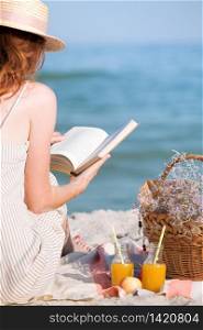 Summer - picnic by the sea. Girl in Hat read book and basket for a picnic with buns, apples and juice.
