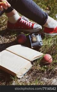Summer - picnic in the meadow. girl on a picnic. legs in sneakers, book, peaches and a retro camera in the frame