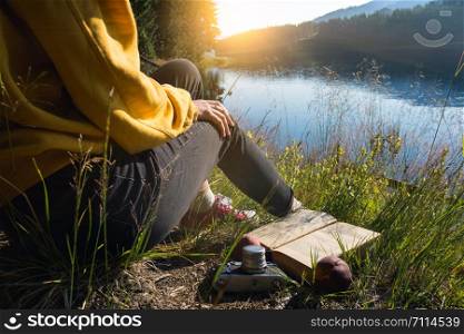 Summer - picnic in the meadow. girl on a picnic by the lake. legs in sneakers, book, peaches and a retro camera in the frame