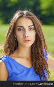 Summer portrait of a beautiful young brunette Caucasian girl in blue dress outdoors in the park