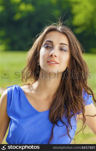 Summer portrait of a beautiful young brunette Caucasian girl in blue dress outdoors in the park