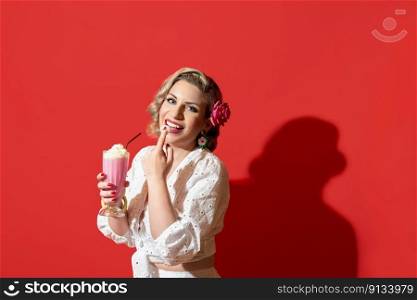 Summer portrait of a blonde woman in a white dress enjoying a strawberry milkshake. Portrait of a happy woman with curly hair and a summer dress, isolated on a red background