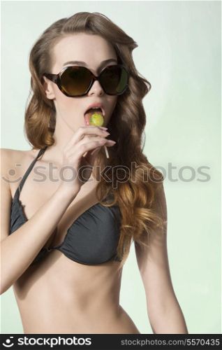 summer portrait of sexy female with bikini and sunglasses eating in sensual mode lollipop