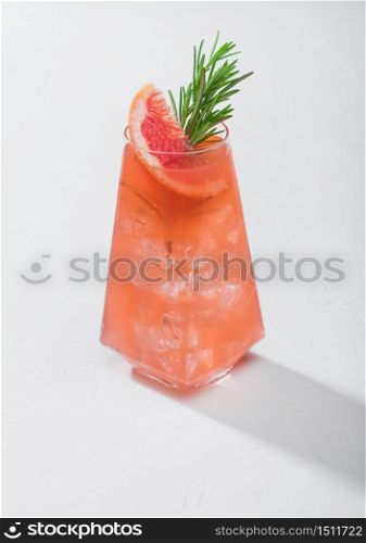 Summer red grapefruit cocktail in modern luxury highball glass with fruit slice and rosemary on white background. Hard light