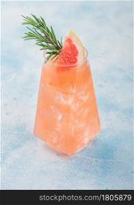 Summer red grapefruit cocktail in modern luxury highball glass with fruit slice and rosemary on light blue background.